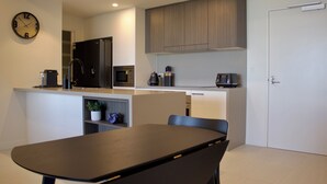 A modern kitchen with a dining area, featuring a clock, a microwave, a coffee machine, and a sink. - RIVERVIEWS@The Cosmopolitan Unit 20805 (Sunshine Coast)