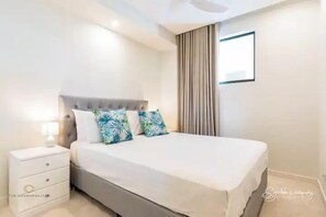 A modern bedroom with a large bed, a bedside table, and a window with curtains. - RIVER FRONT AND OCEAN VIEW 2 BEDROOM DELUXE UNIT IN AN EXCLUSIVE COMPLEX (Sunshine Coast)
