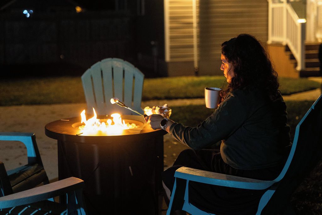 A person sitting by a fire pit with a chair and a table, outdoors at night.