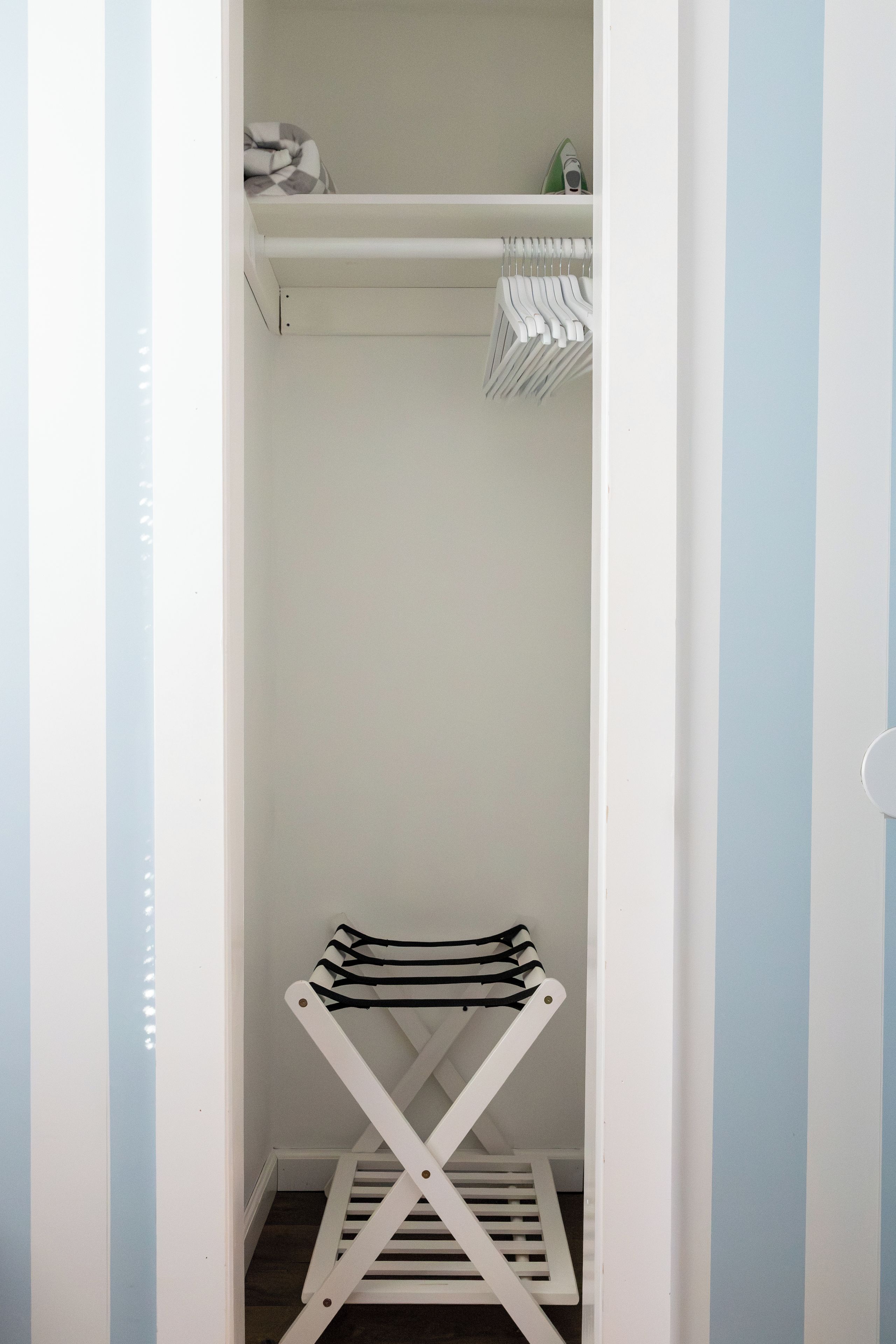 A narrow walk-in closet with a white shelving unit and a drying rack.