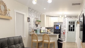Una sala de estar moderna con un sofá de cuero negro, una mesa de centro blanca y un televisor sobre un mueble.