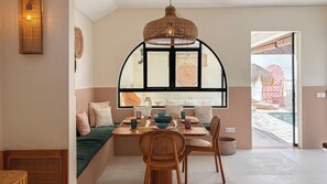Un comedor acogedor con una mesa preparada para dos, una silla de mimbre y vistas a través de un amplio ventanal.