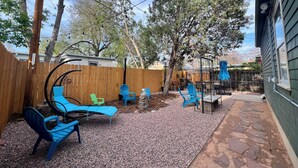 Un jardin avec une clôture en bois, des chaises bleues, une pergola et un espace patio dallé de pierres.