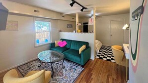 Un espace de vie compact avec un canapé vert, une petite table ronde, un sol à carreaux et un miroir au mur.