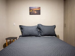 A bedroom with a bed, pillows, a nightstand, a wall-mounted painting, and a door. - Parques Guadalajara Department Condominium, Central, Comfortable (Guadalajara)