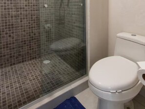 Une salle de bain avec une douche à parois de verre, des toilettes blanches et un tapis de bain bleu.