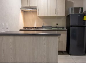 A kitchen with light wood cabinets, a black refrigerator, and a stainless steel range hood.