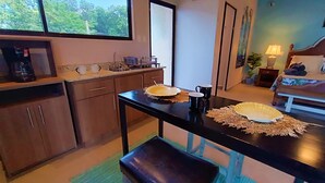 A compact kitchen with a window, a coffee machine, and a dining area with a table set for two. - Suite Dream Blue Tu Descanso Soñado! Tamarindo Costa Rica (Provincia de Guanacaste)
