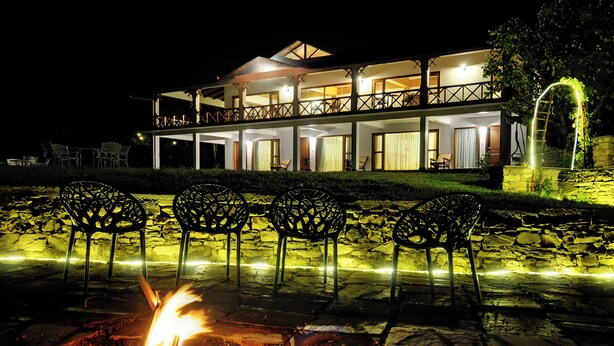 A two-story building with a balcony, outdoor seating, and a fire pit. - Dyo - The Organic Village Resort (Dhari)