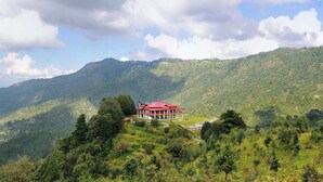 A building with a red roof surrounded by lush green hills and a clear sky. - Dyo - The Organic Village Resort (Dhari)