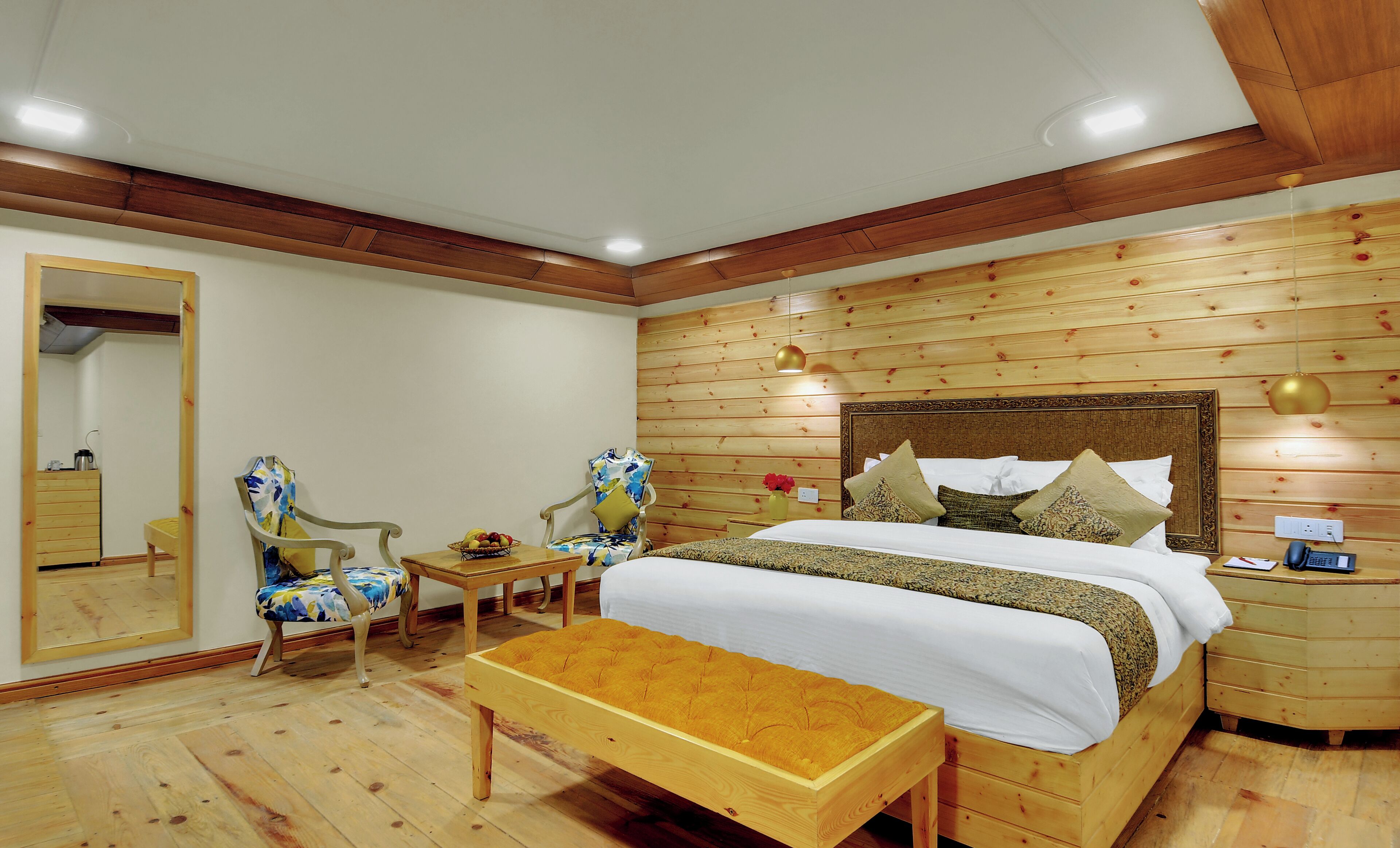 A wooden-paneled bedroom with a bed, two chairs, a small table, and a bench.