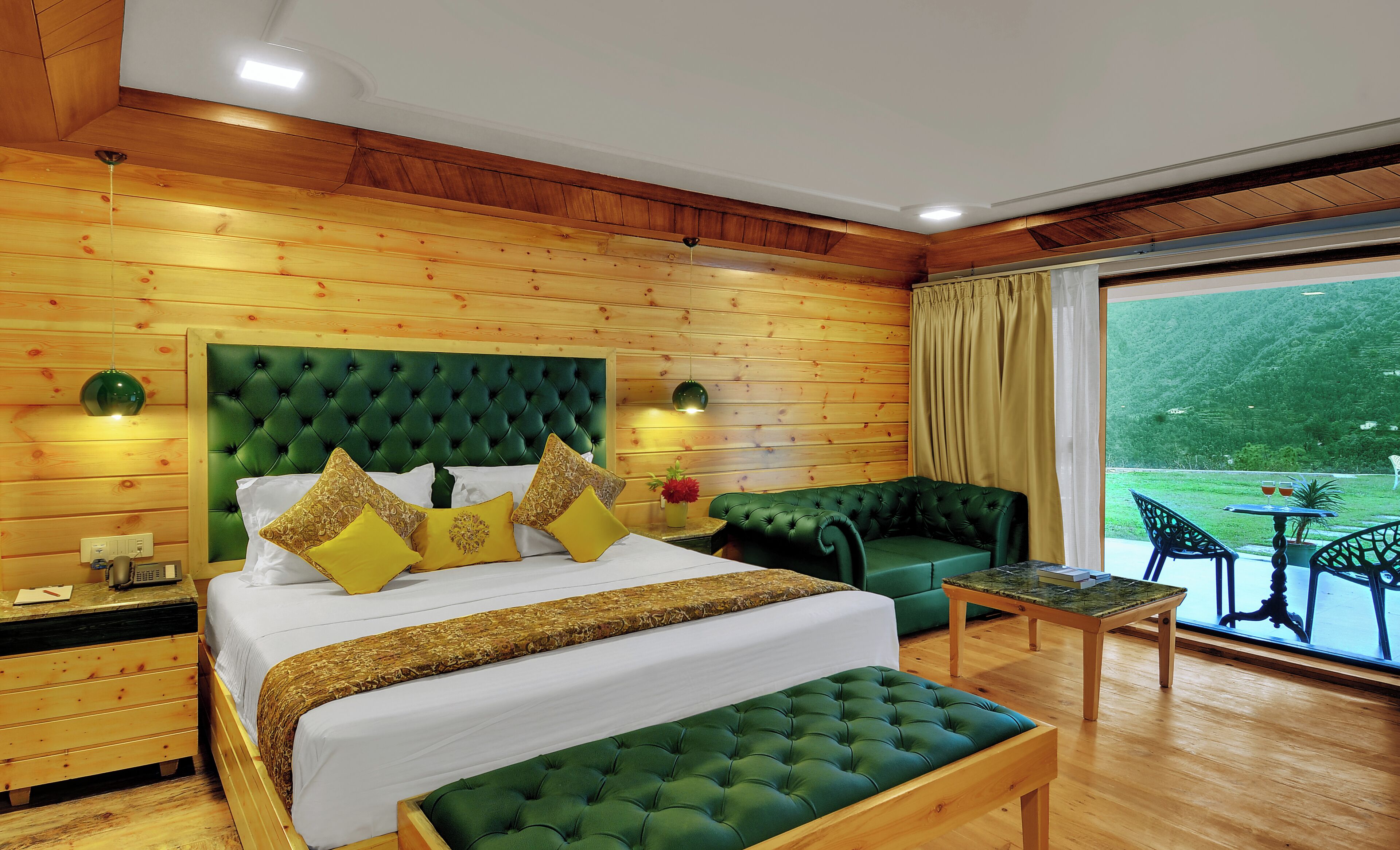 Habitación de hotel con una cama grande, un sofá verde, una mesita y vistas al exterior.