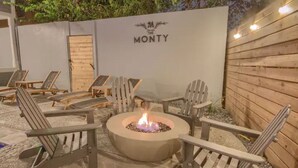 Un área de estar al aire libre con sillas Adirondack y una chimenea central.
