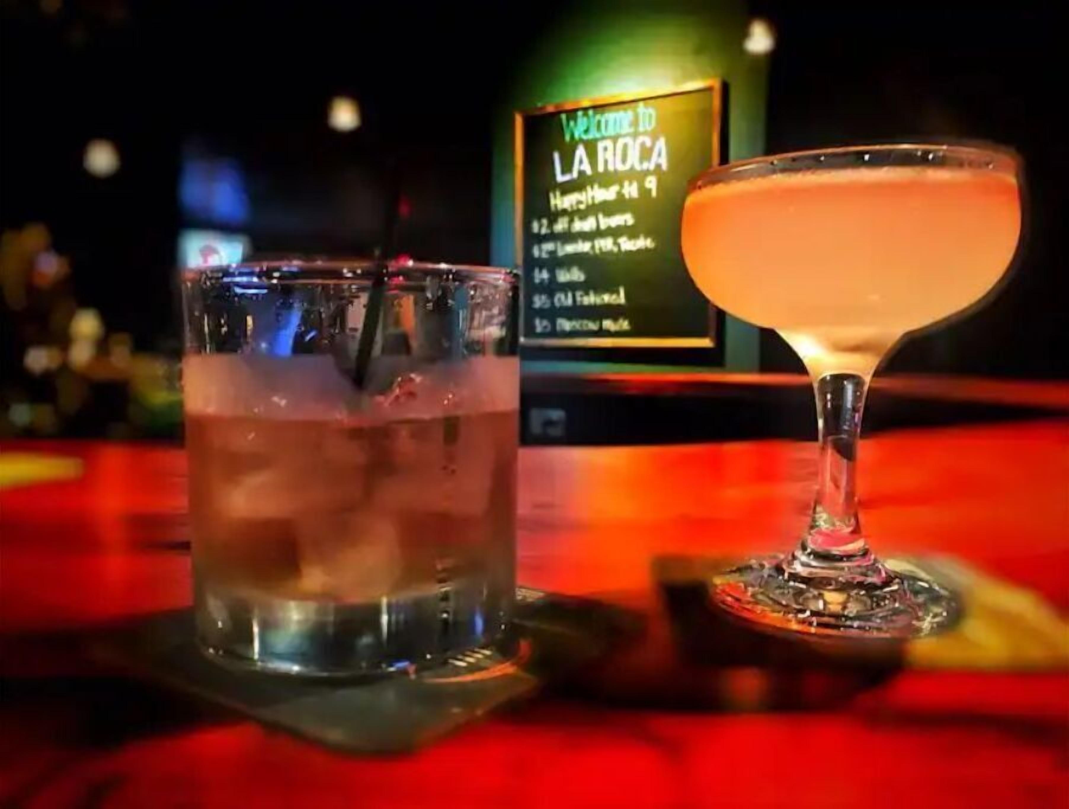 Two drinks on a bar counter with a sign in the background.