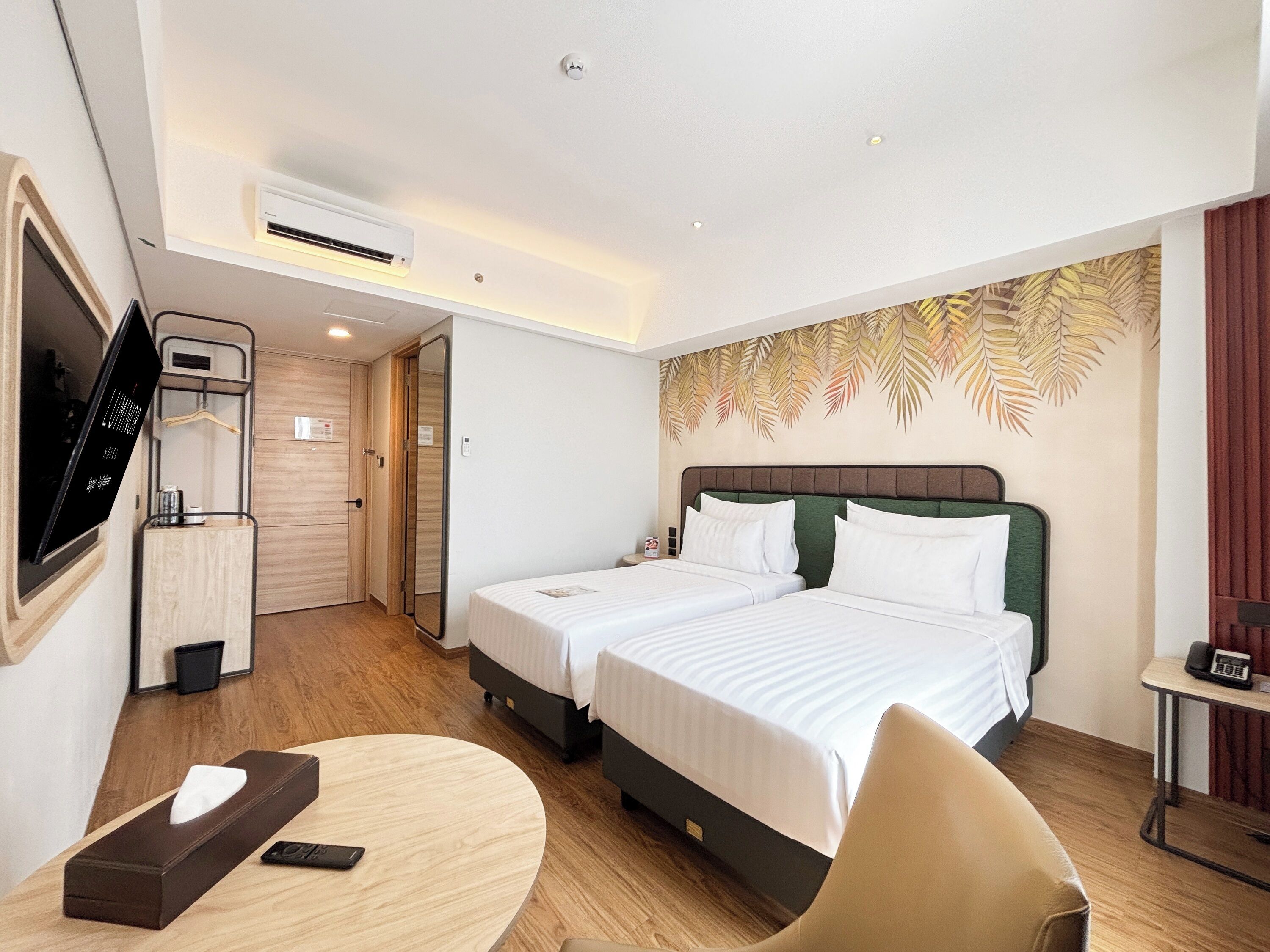 A hotel room with two beds, a TV, a desk, and a mirror.