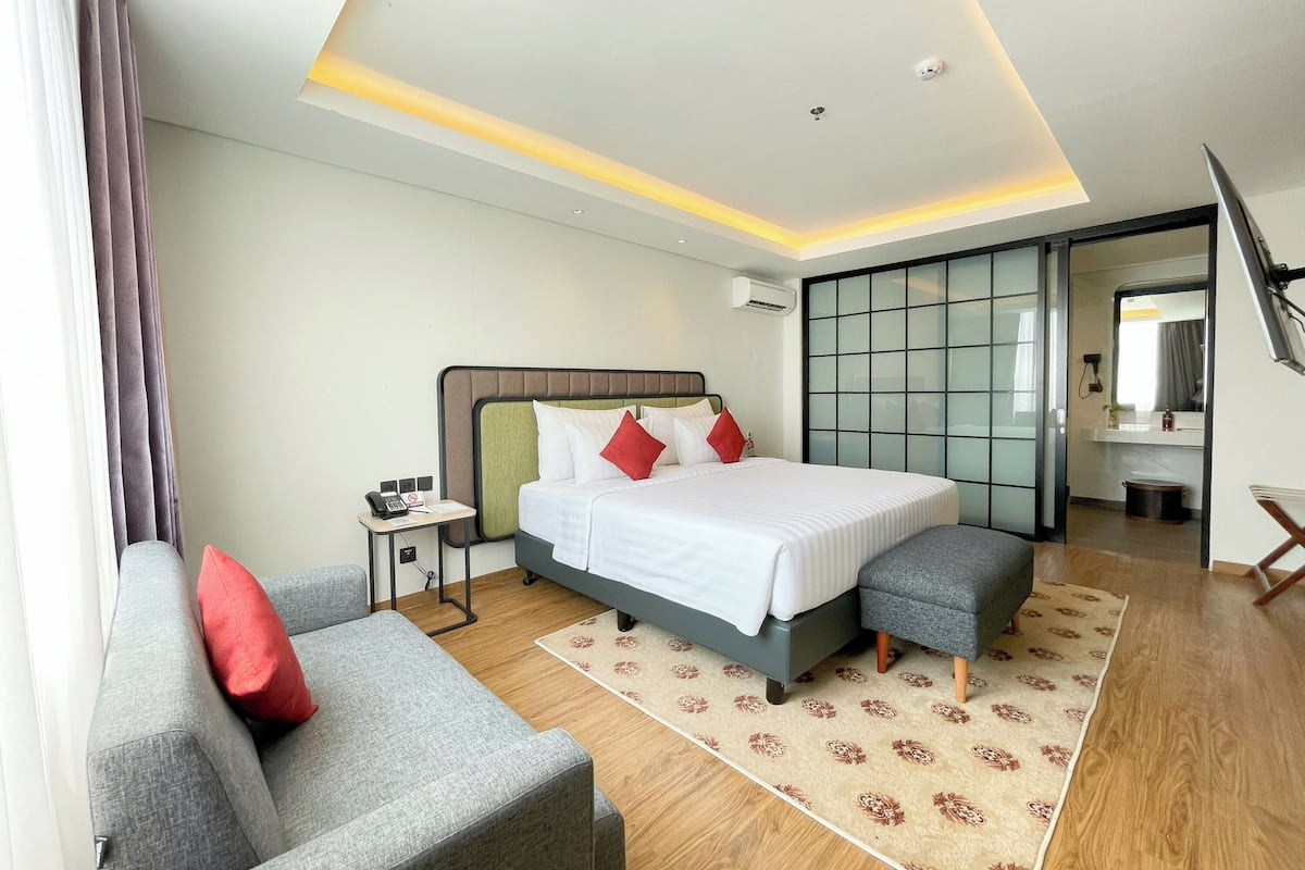A modern hotel room with a large bed, a desk, a chair, and a sofa.