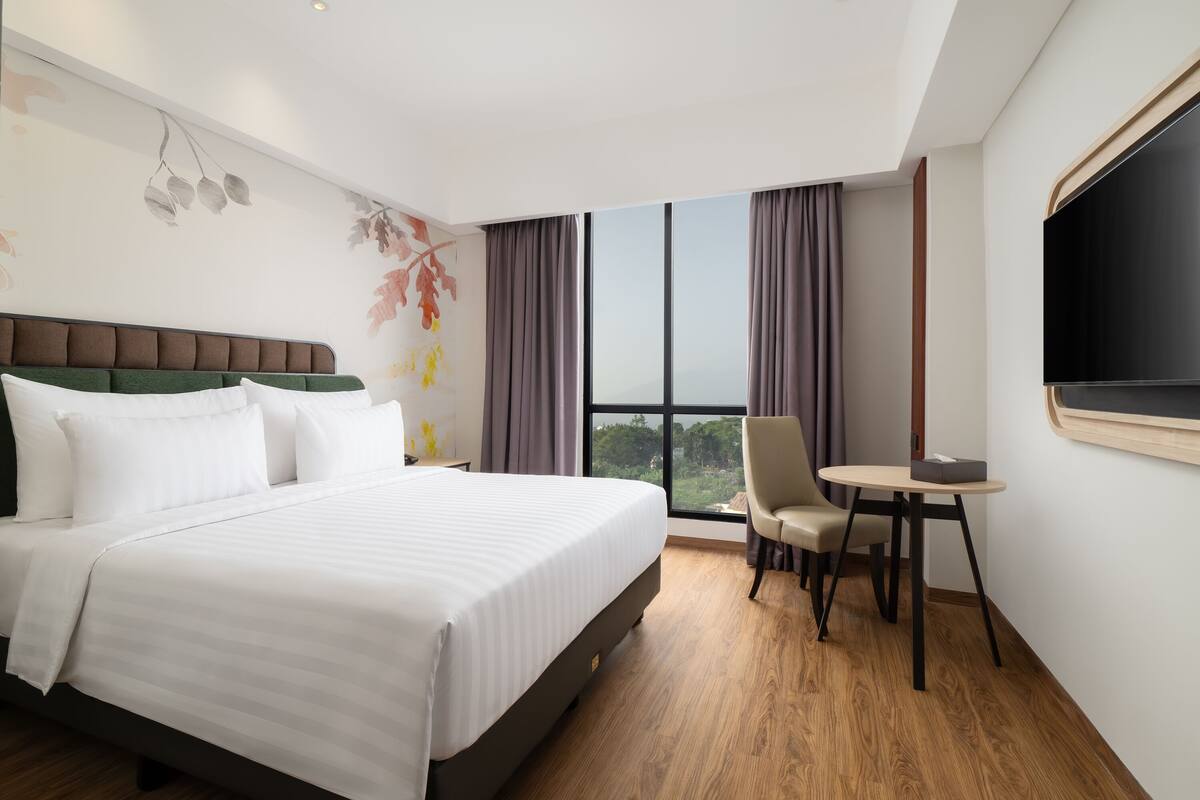 A hotel room with a large bed, a desk, a chair, and a TV.