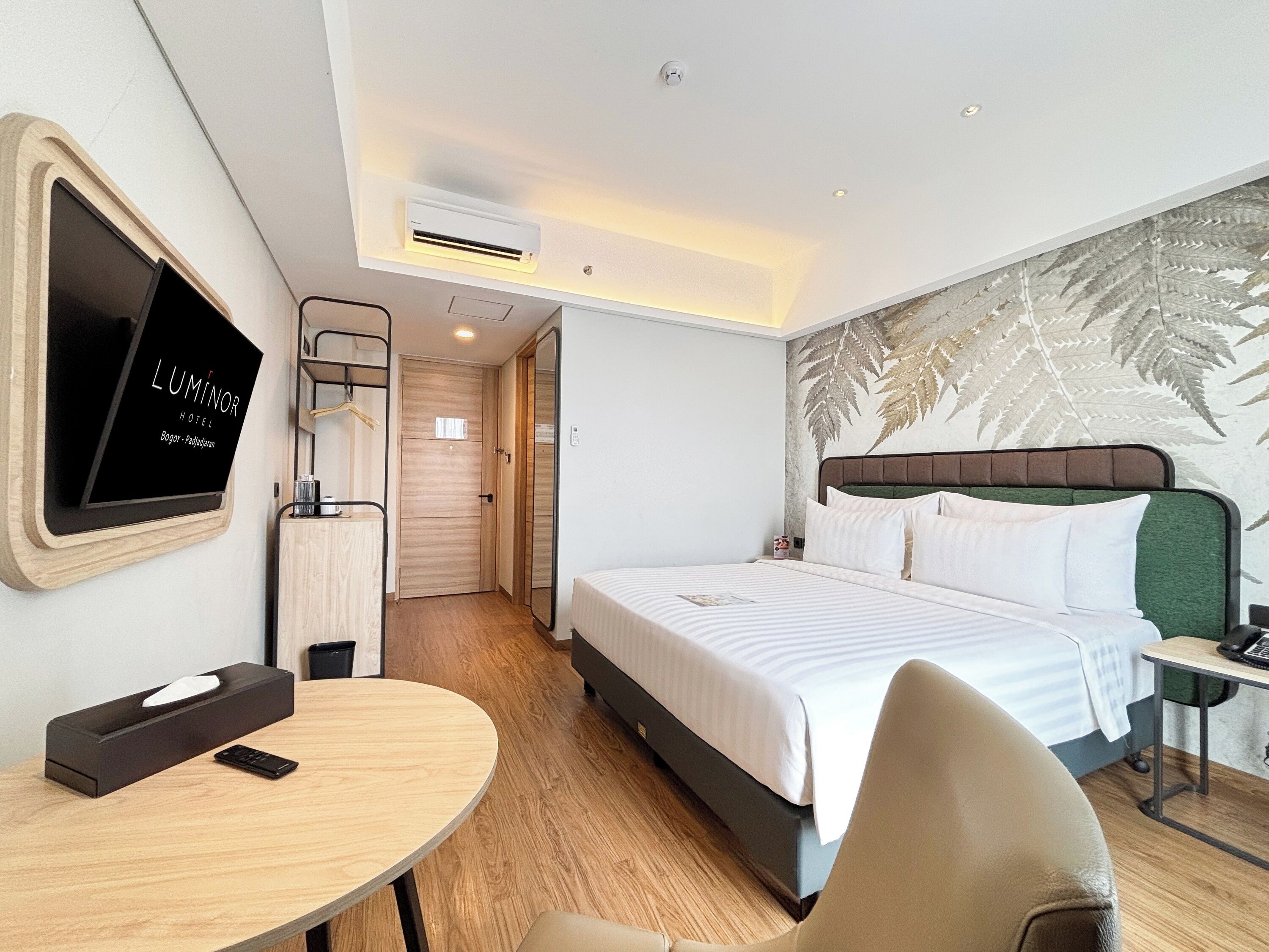 A hotel room with a bed, a desk, a chair, a TV, and a wall-mounted air conditioner.