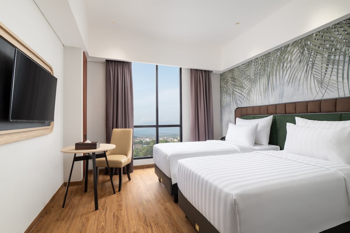 A hotel room with a large bed, a desk, a chair, a TV, and a window with a city view.