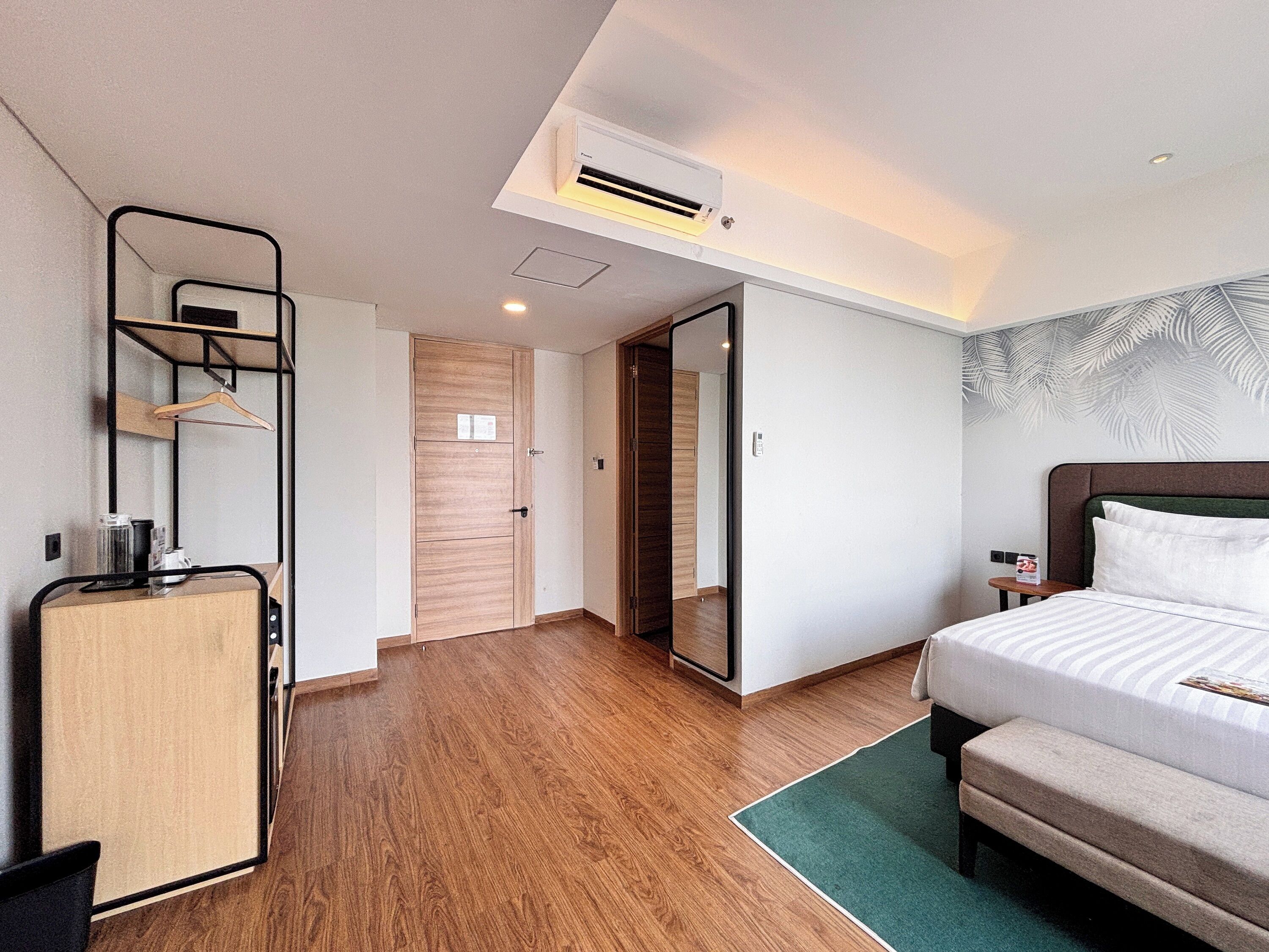 A hotel room with a bed, a desk, a mirror, and a wardrobe.
