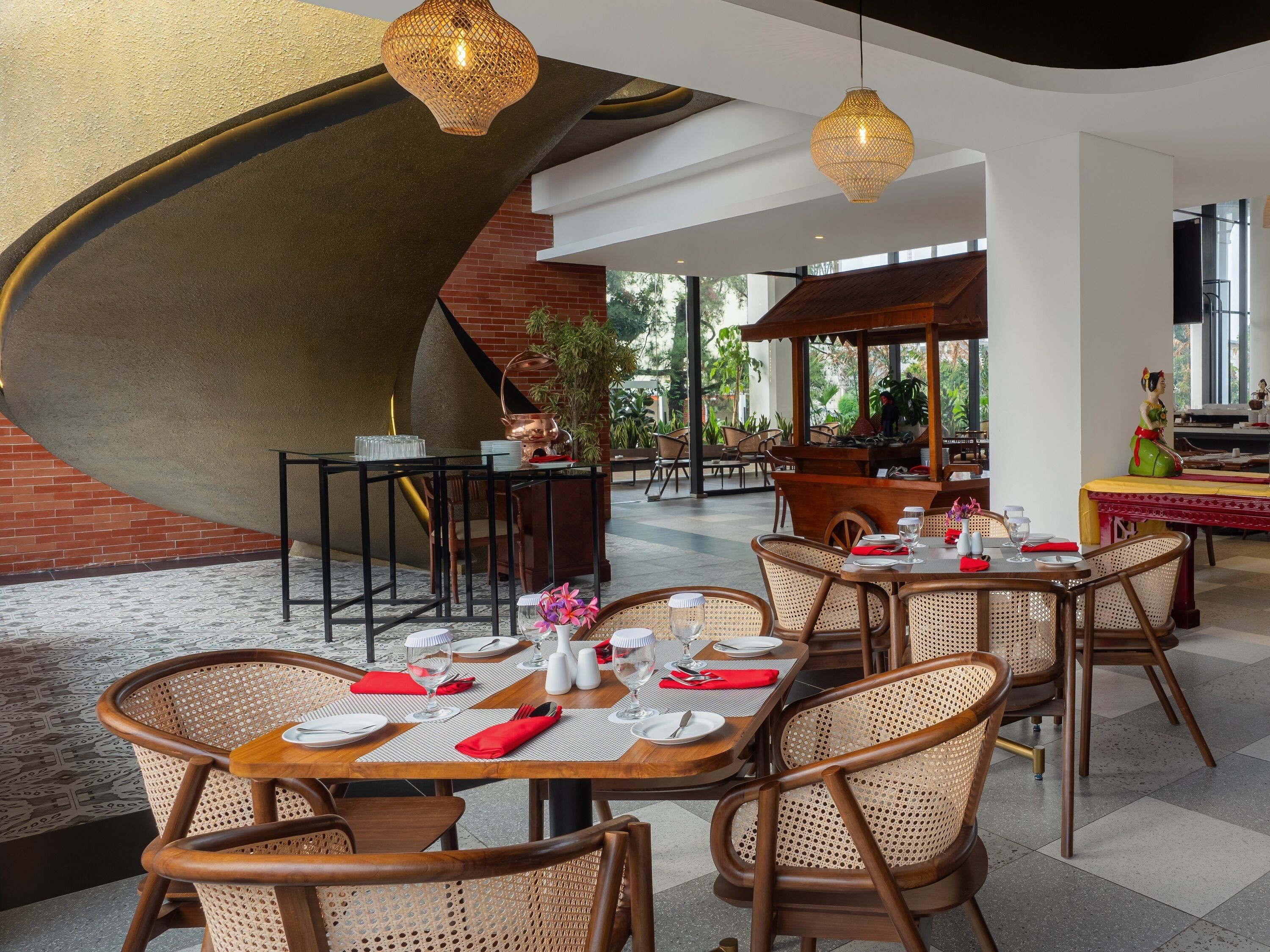 Un restaurant avec des tables rondes, des chaises en osier et des lampes suspendues.