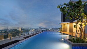 Un hotel moderno con piscina infinita en la azotea, vistas a la ciudad y una entrada bien iluminada.