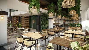 Un interior de restaurante moderno con mesas y sillas de madera, plantas colgantes e iluminación colgante de mimbre.