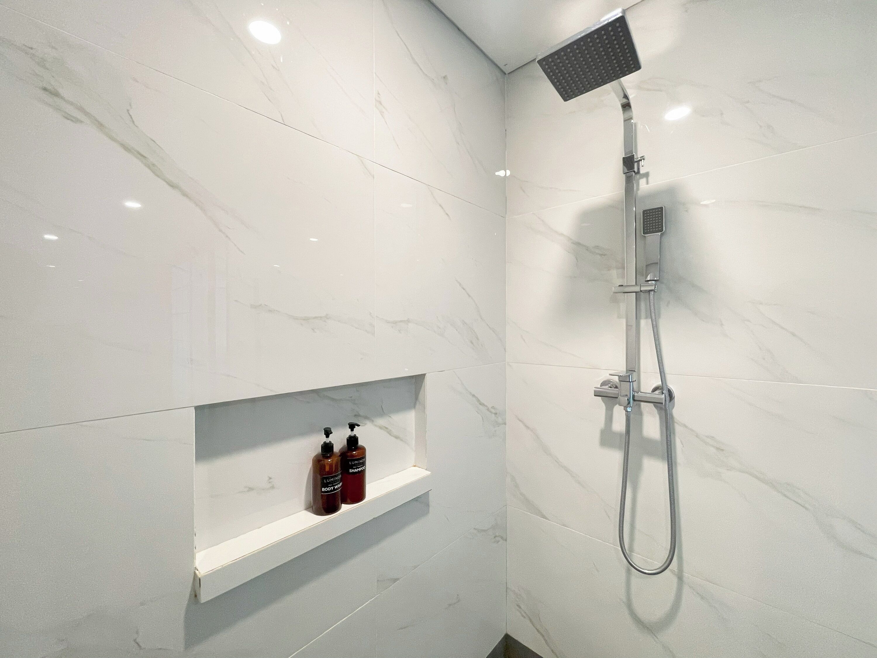 Une salle de bain moderne avec une douche, une étagère contenant des articles de toilette et des murs en marbre.