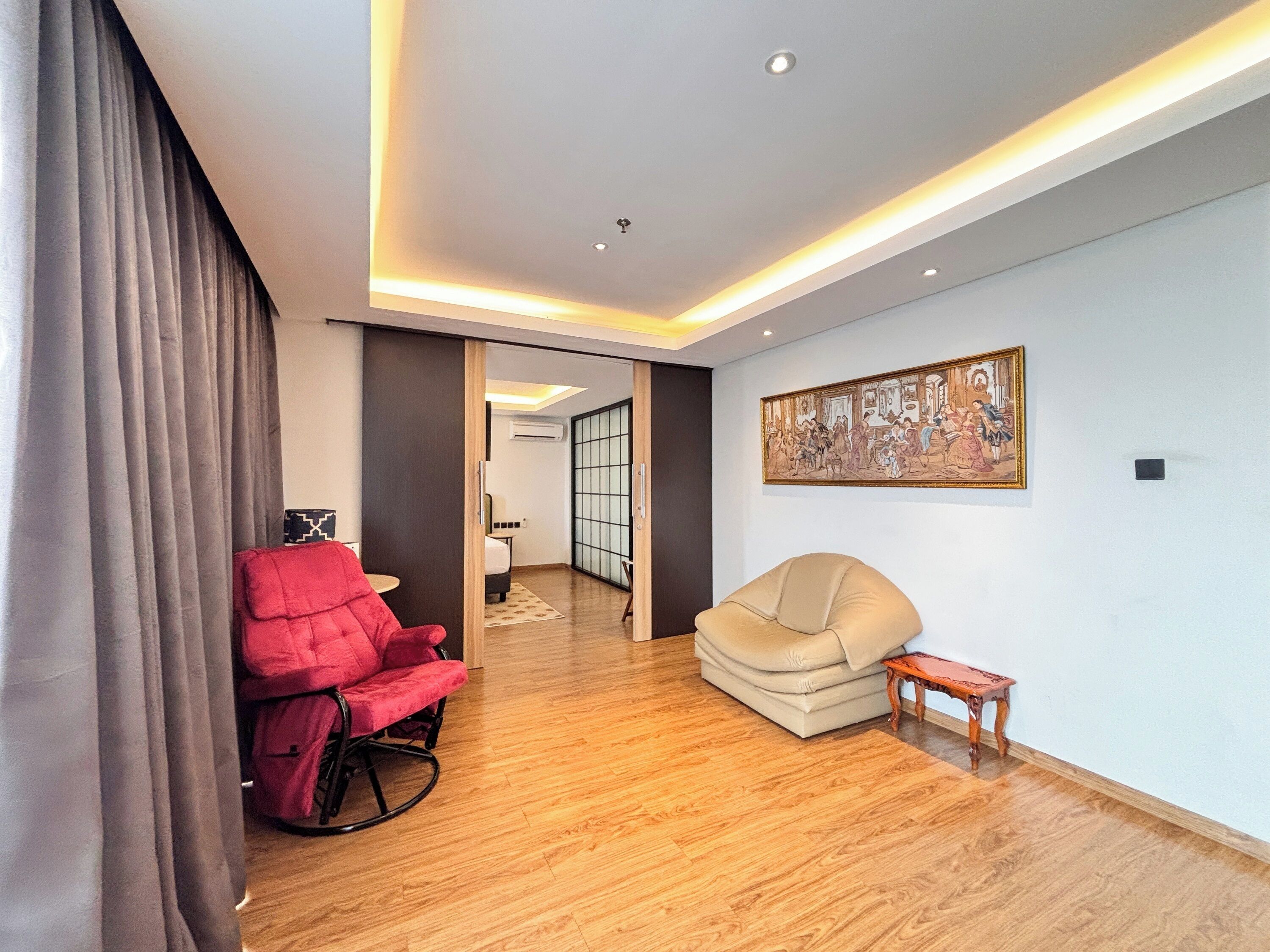 Uma sala de estar moderna com uma poltrona reclinável vermelha, um sofá bege e uma pequena mesa de madeira.