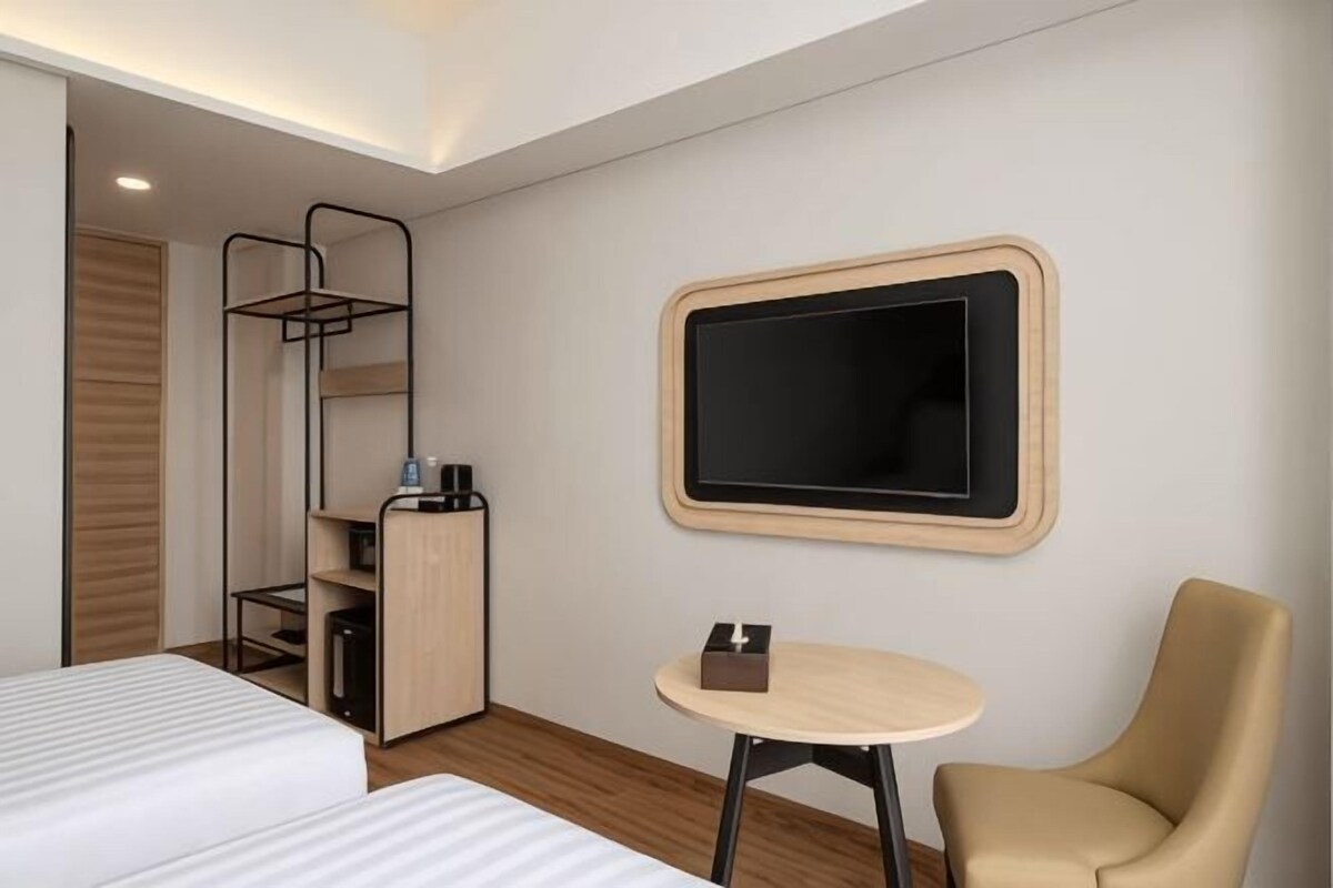 A hotel room with two beds, a desk, a chair, a TV, and a wardrobe.