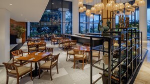 Un comedor amplio con mesas y sillas de madera, una zona de bar central con adornos, y grandes ventanales que ofrecen vistas al exterior.