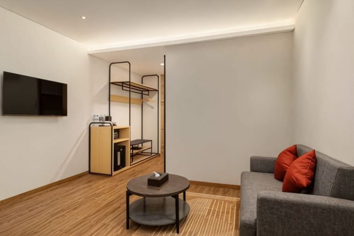 Habitación de hotel moderna con literas, un televisor de pantalla plana, una mesita pequeña y un sofá con cojines rojos.