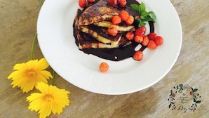 Un plato de tortitas con fresas y salsa de chocolate sobre una mesa de madera.