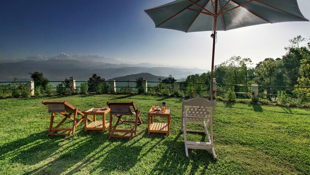 Un espacio al aire libre con asientos de césped, muebles de madera y un gran paraguas, con vistas a un paisaje montañoso.