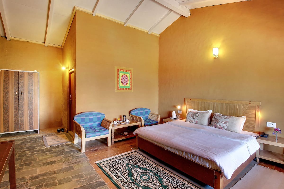 A bedroom with a large bed, two chairs, a nightstand, a wooden wardrobe, and a decorative wall hanging.
