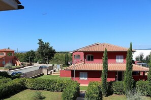 A red two-story house with a tiled roof, surrounded by greenery and other houses.