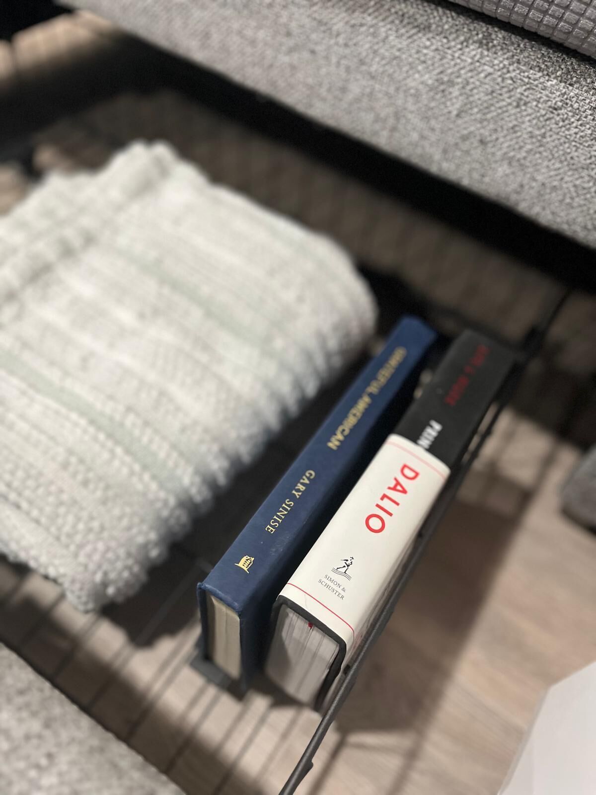 A close-up of a bookshelf with books and a white knitted blanket.