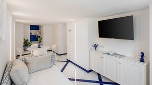 Ein modernes Wohnzimmer mit einer Couch, einem Essbereich mit Tisch und Stühlen, einer Küchenzeile mit Schränken und einem an der Wand befestigten Fernseher.