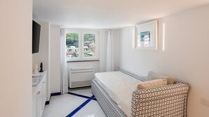 Ein Schlafzimmer mit Bett, einem Fenster mit Vorhängen, einem Heizkörper und einem Bild an der Wand.