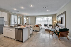 A modern kitchen with a central island, a dining area with a sofa and chairs, and a living room with a TV and seating. - Luxury 5 bedroom home, 10 minutes from Disney (Kissimmee)