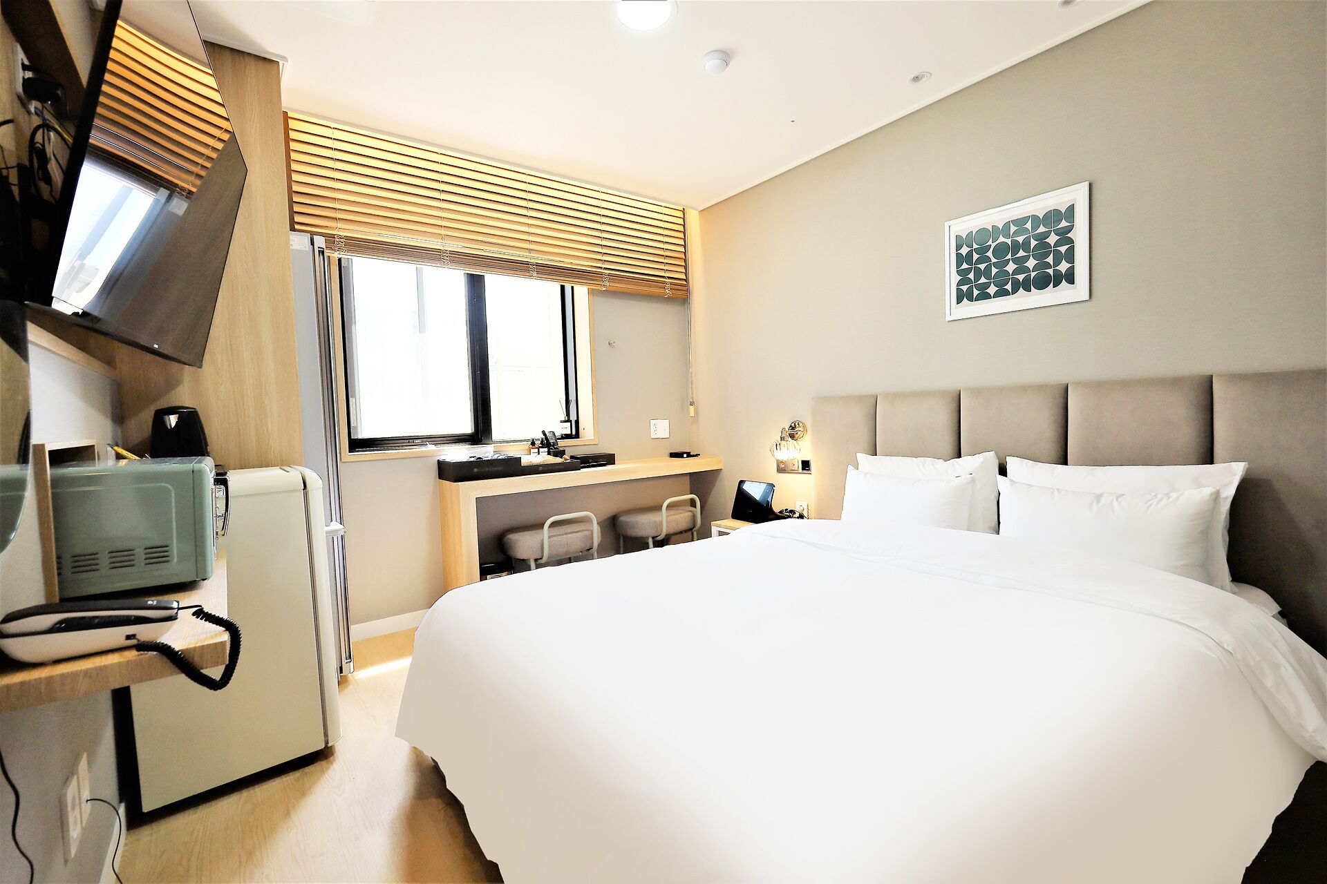 A hotel room with a bed, a desk, a chair, a television, and a window with blinds.