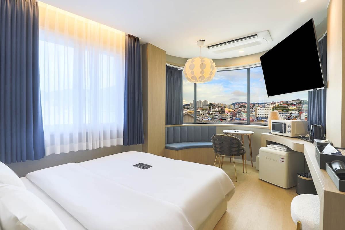 A hotel room with a bed, a desk with a microwave, a chair, and a TV.