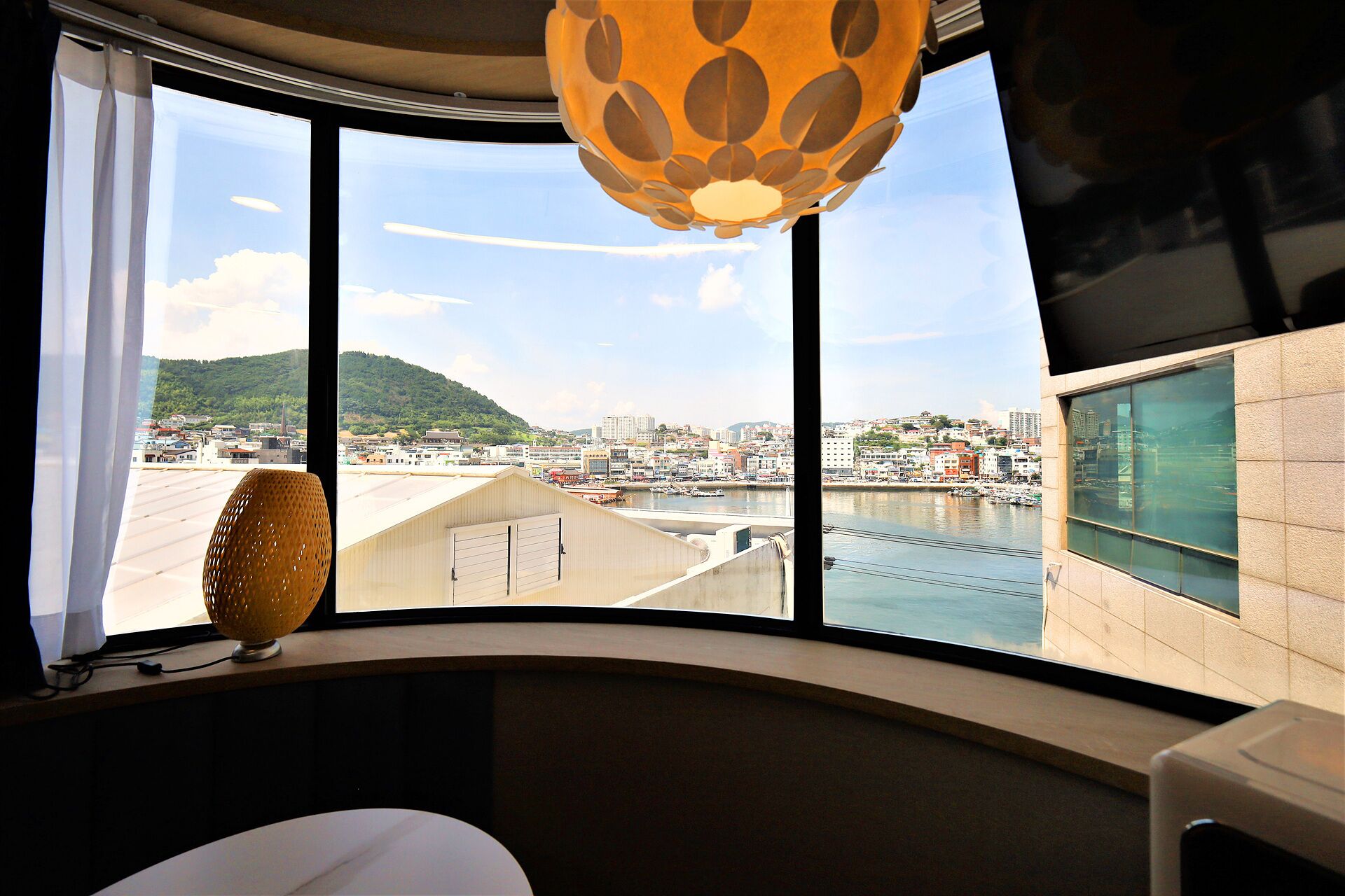 Una habitación con un ventanal grande, una lámpara y vistas a la ciudad y al agua.