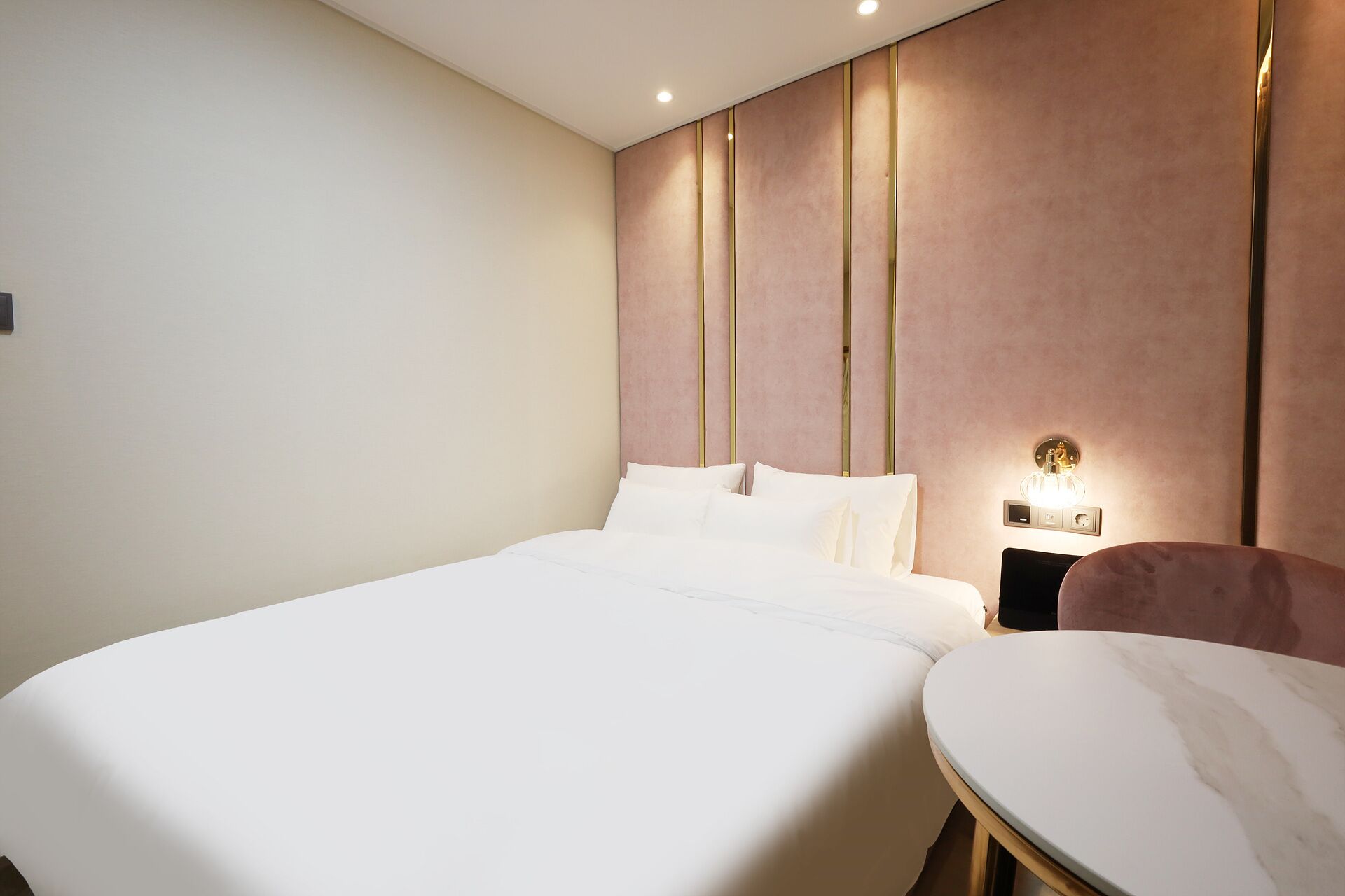 Una habitación de hotel con una cama grande, una mesa redonda y una mesita de noche con lámpara.