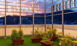 A balcony with potted plants, a view of a cityscape, and a large window with the word 'HOTEL' visible. - DELAMOUR Hotel (Tongyeong)