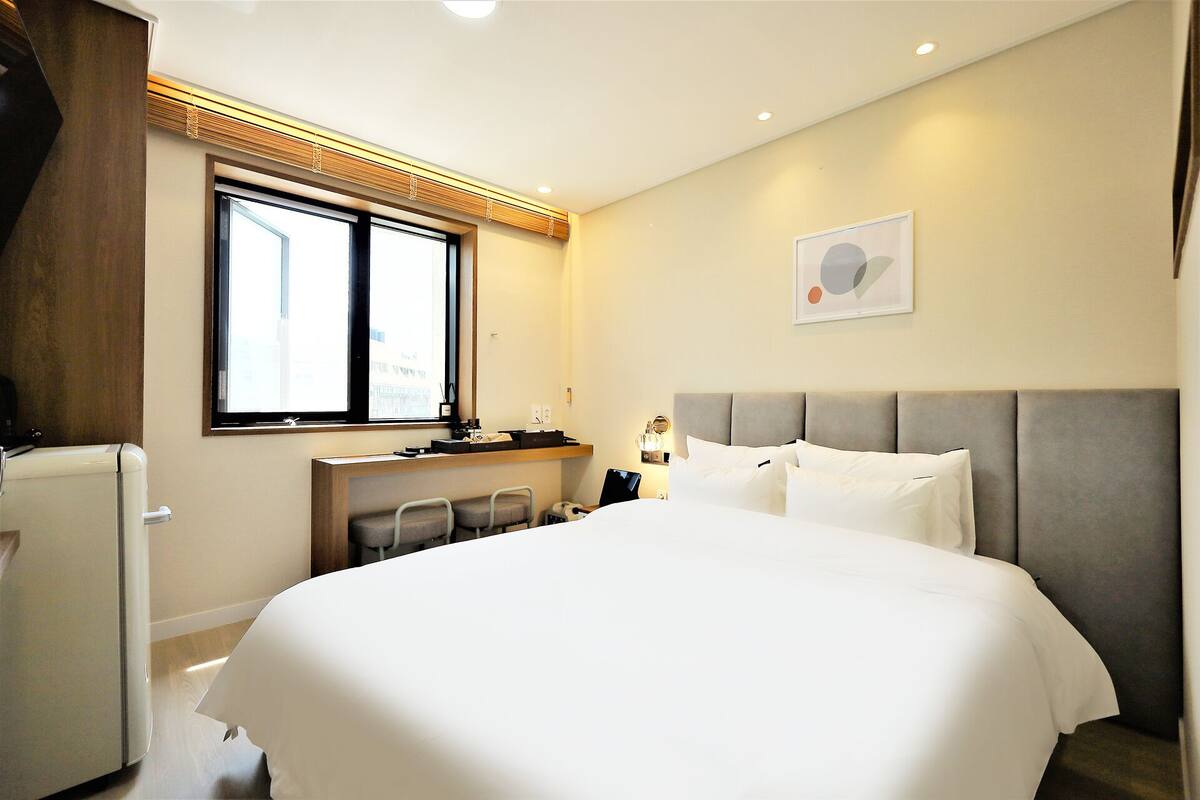 A hotel room with a bed, a desk, a chair, a window, and a wall-mounted artwork.