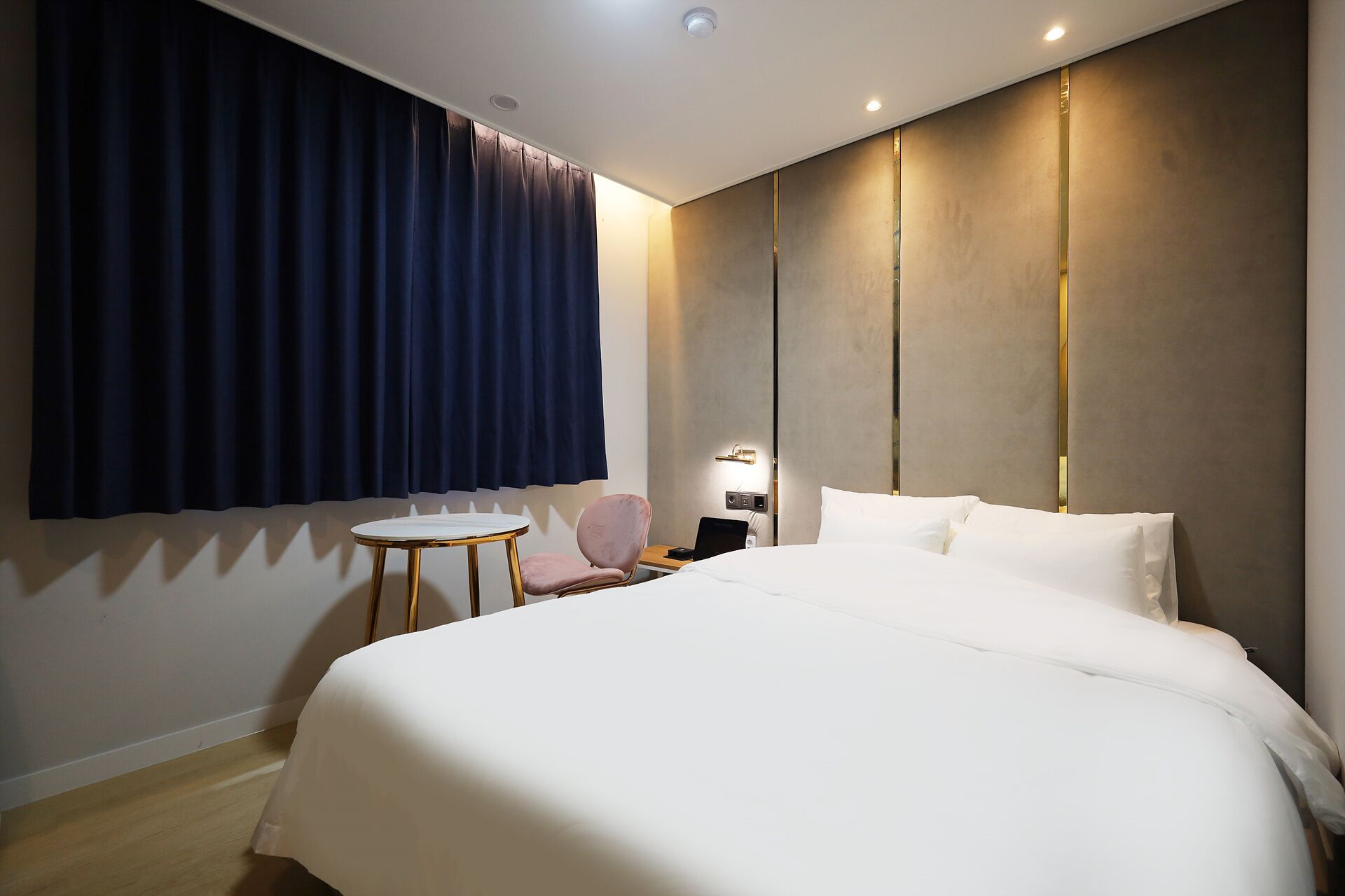 A hotel room with a large bed, a small round table, a chair, and a desk with a laptop.