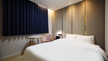 A hotel room with a large bed, a small round table, a chair, and a desk with a laptop.