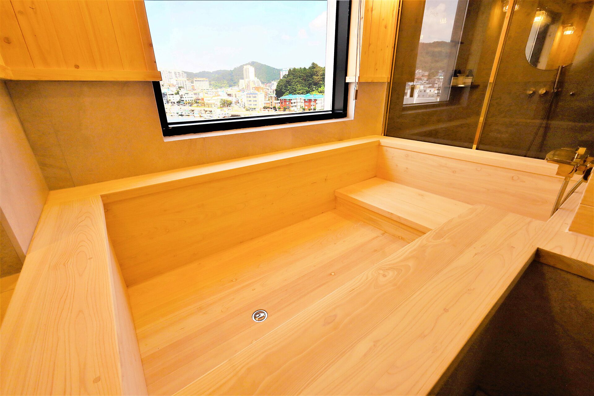 A wooden bathtub with a window, a sink, and a mirror.