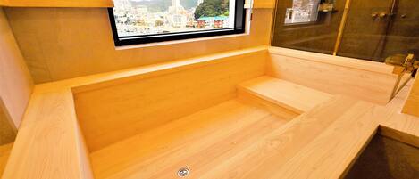 A wooden bathtub with a window, a sink, and a mirror.